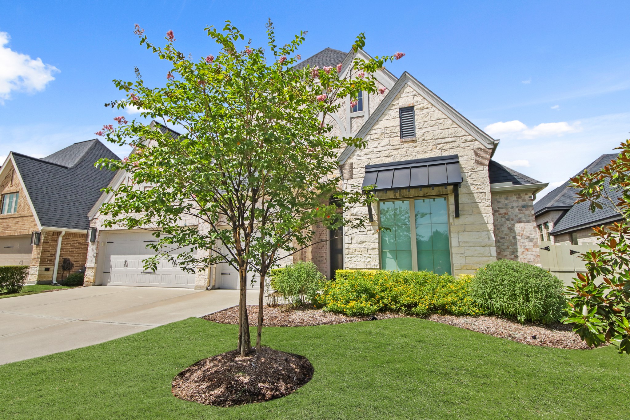 17406 Bayflower Conroe, TX 77385 - Photo 2 of 35 Well-maintained front yard featuring a beautiful landscaping. The house includes a three-car garage and a sleek black awning over a large front window.
