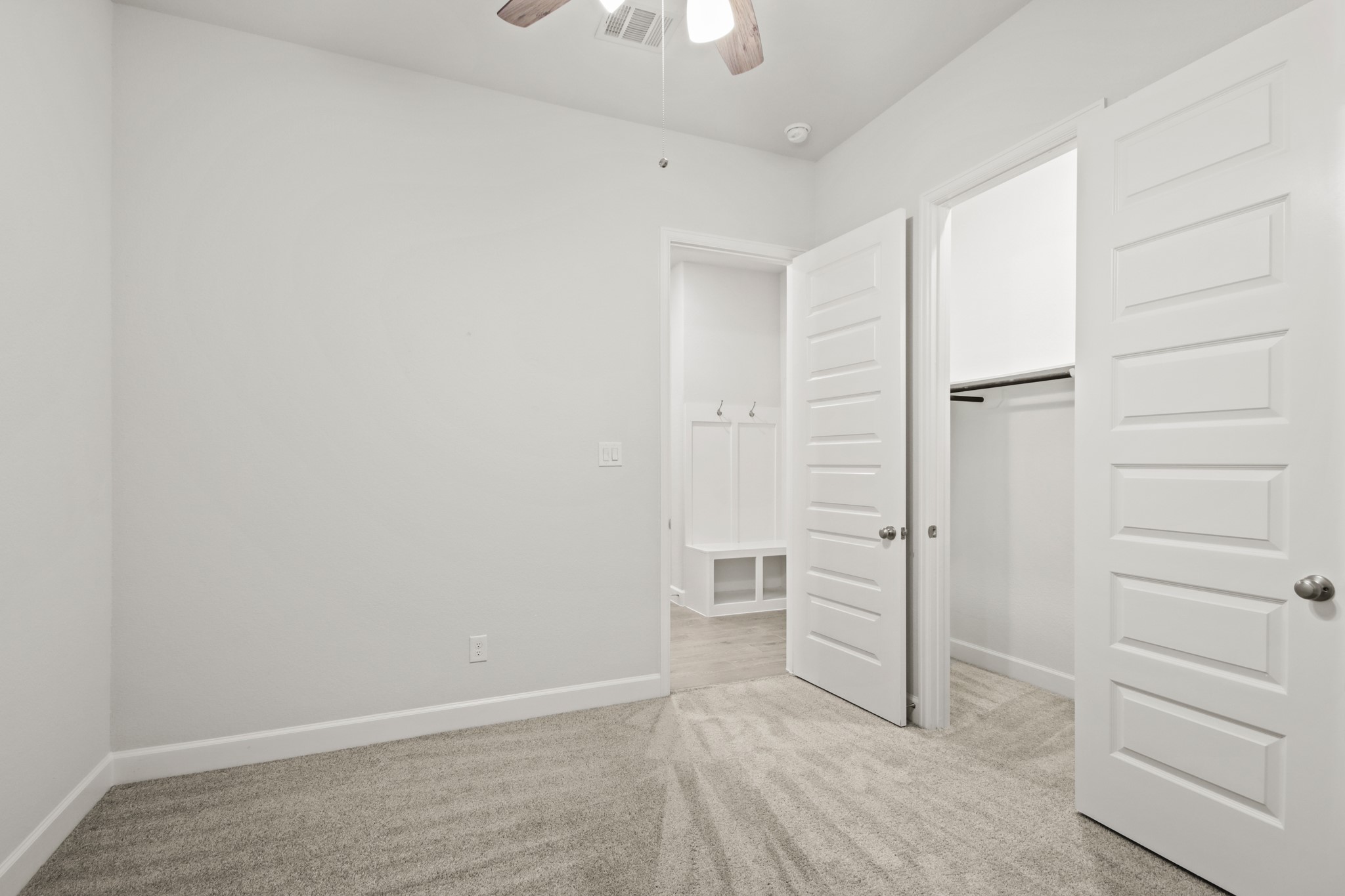 17406 Bayflower Conroe, TX 77385 - Photo 21 of 35 Bright, carpeted secondary bedroom with neutral walls and a ceiling fan features a closet with white paneled doors and an adjacent entryway to the mudroom and laundry area.