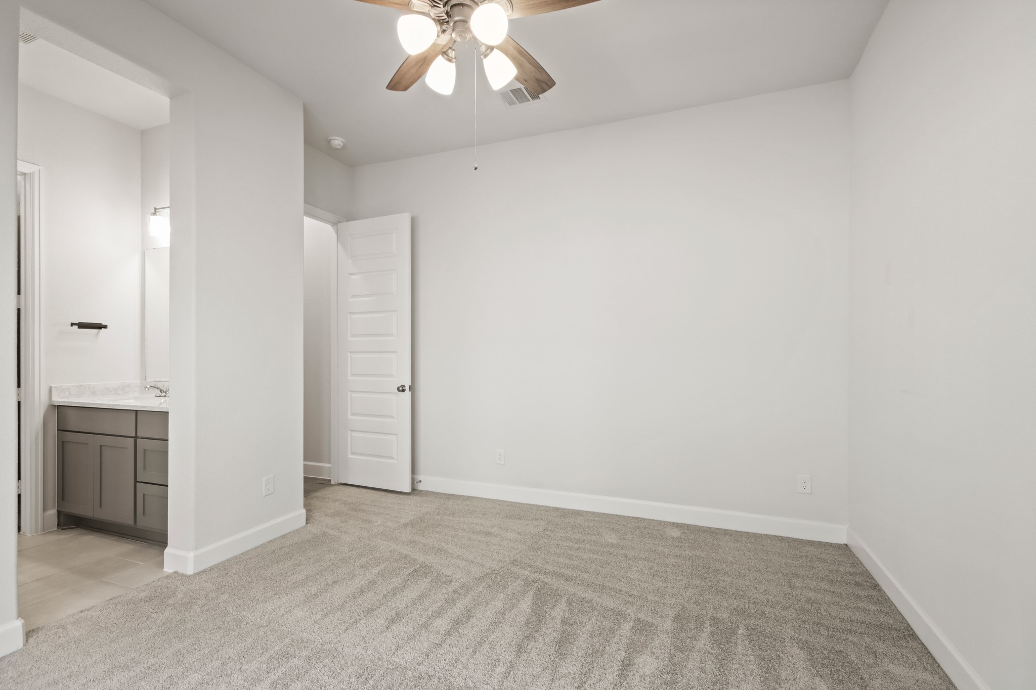 17406 Bayflower Conroe, TX 77385 - Photo 31 of 35 This secondary bedroom features a cozy, carpeted space with neutral walls and a ceiling fan. It includes a doorway leading to a bathroom with a modern vanity and bright lighting, offering convenience and comfort.