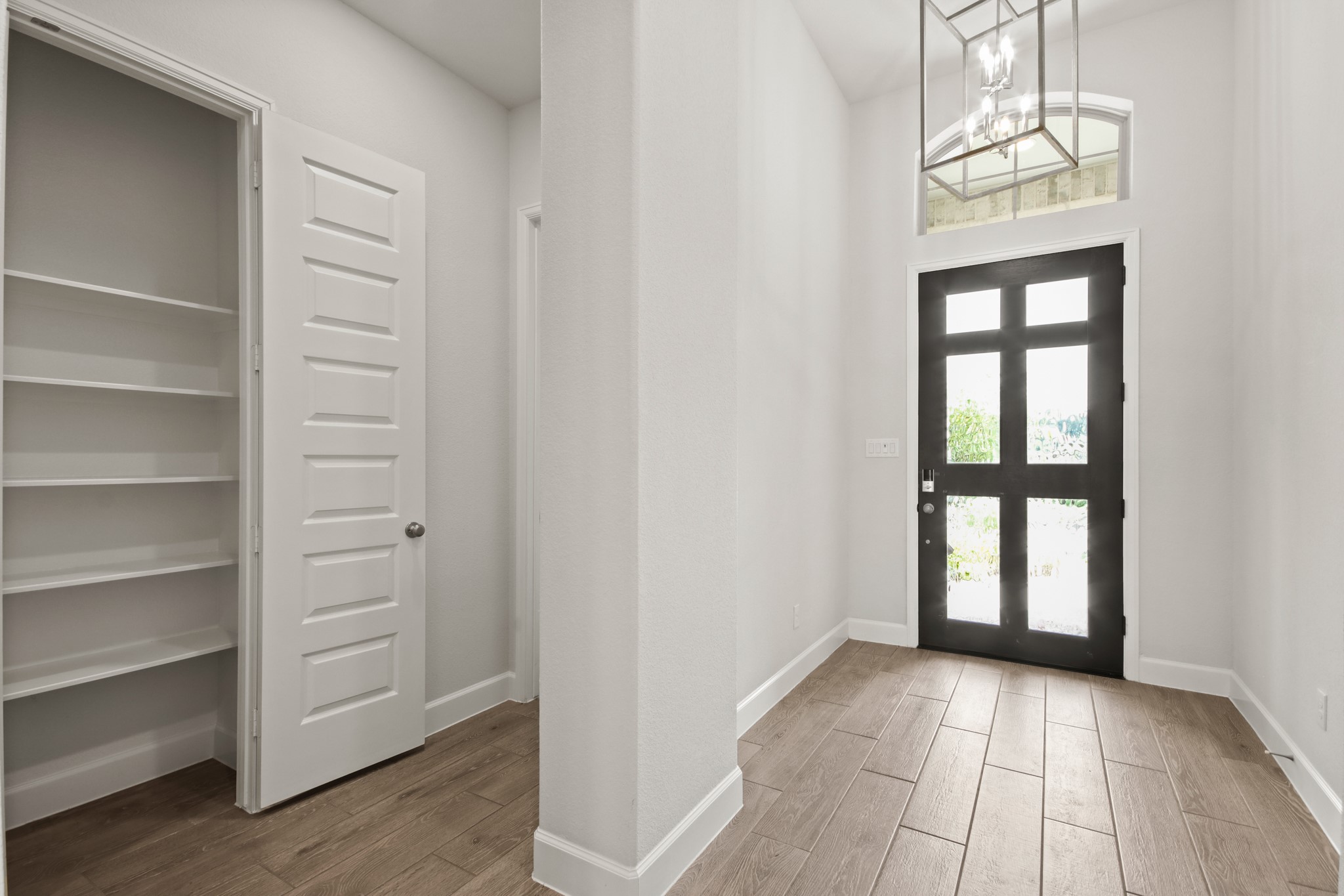 17406 Bayflower Conroe, TX 77385 - Photo 4 of 35 Entryway features a modern black door with glass panels, high ceilings, and a stylish chandelier. It has wood-styled tile flooring, offering a welcoming and functional space.
