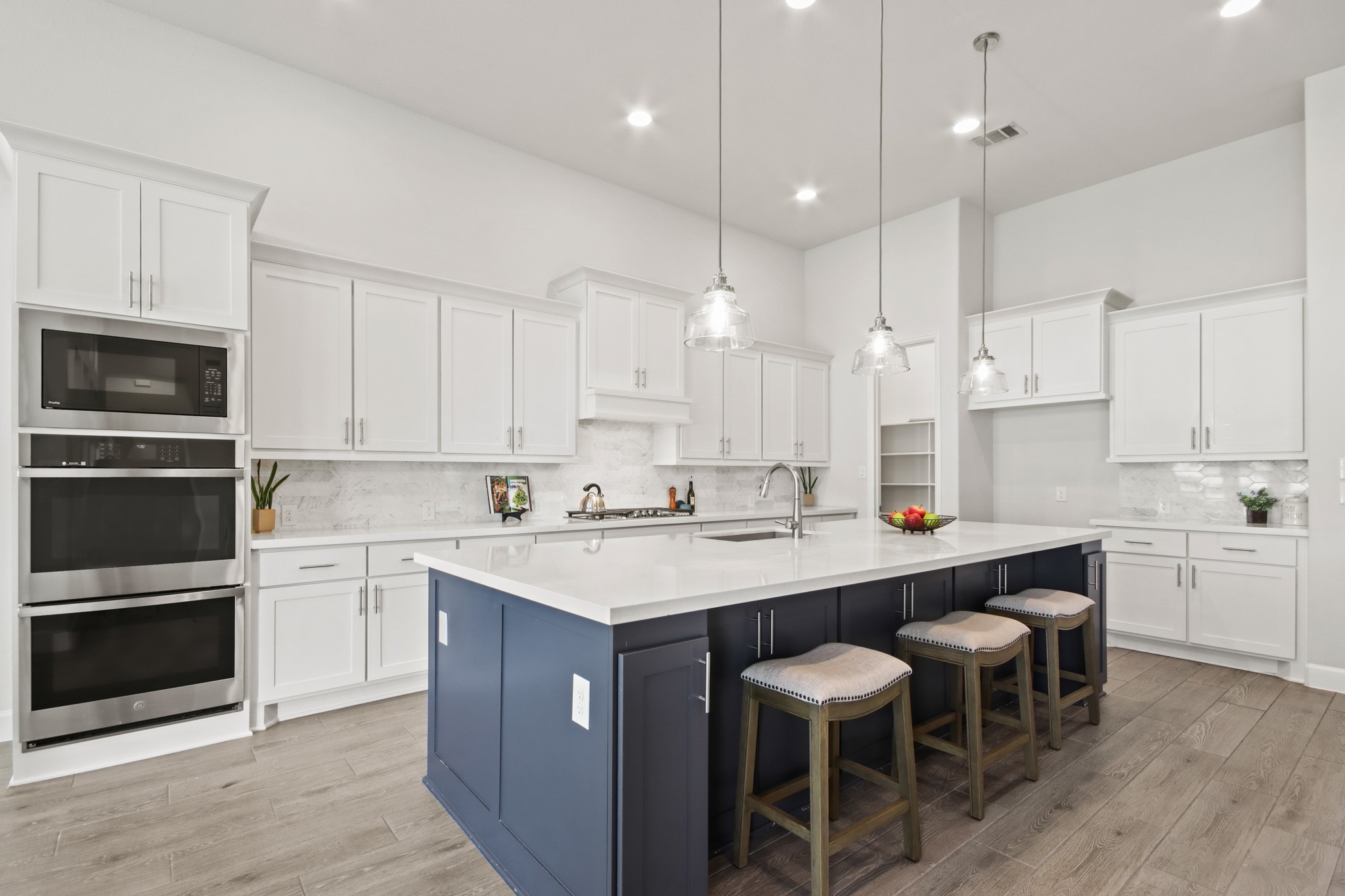 17406 Bayflower Conroe, TX 77385 - Photo 9 of 35 This modern kitchen features sleek white cabinetry, a large island with area for seating, pendant lighting, and stainless steel appliances. The open layout and light wood tile flooring create a spacious and inviting atmosphere.