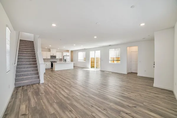 a view of an empty room and a kitchen with wooden floor