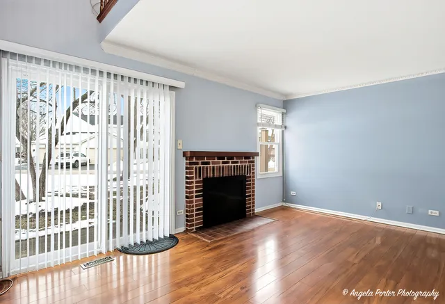 a view of an empty room with wooden floor fireplace and a window