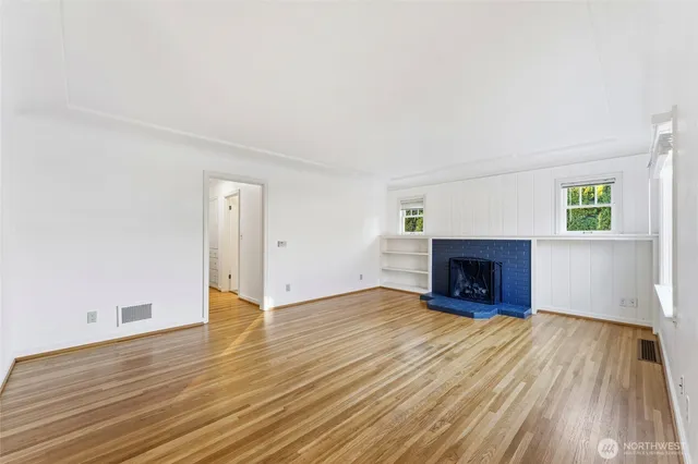 an empty room with wooden floor fireplace and windows