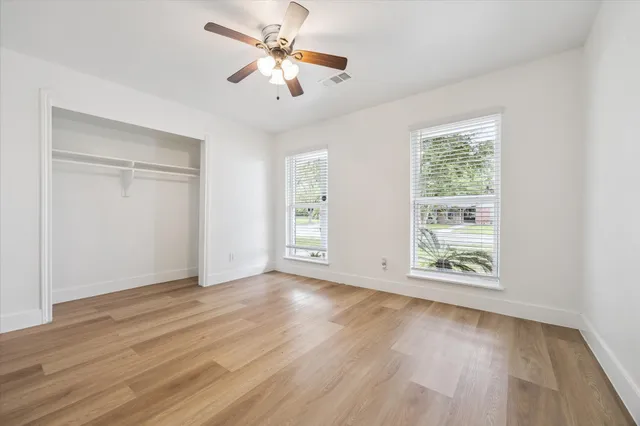 an empty room with wooden floor chandelier fan and windows