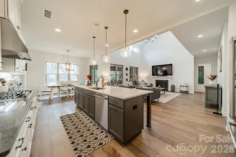 a open kitchen with stainless steel appliances kitchen island granite countertop a stove top oven a sink dishwasher and a fireplace with wooden floor