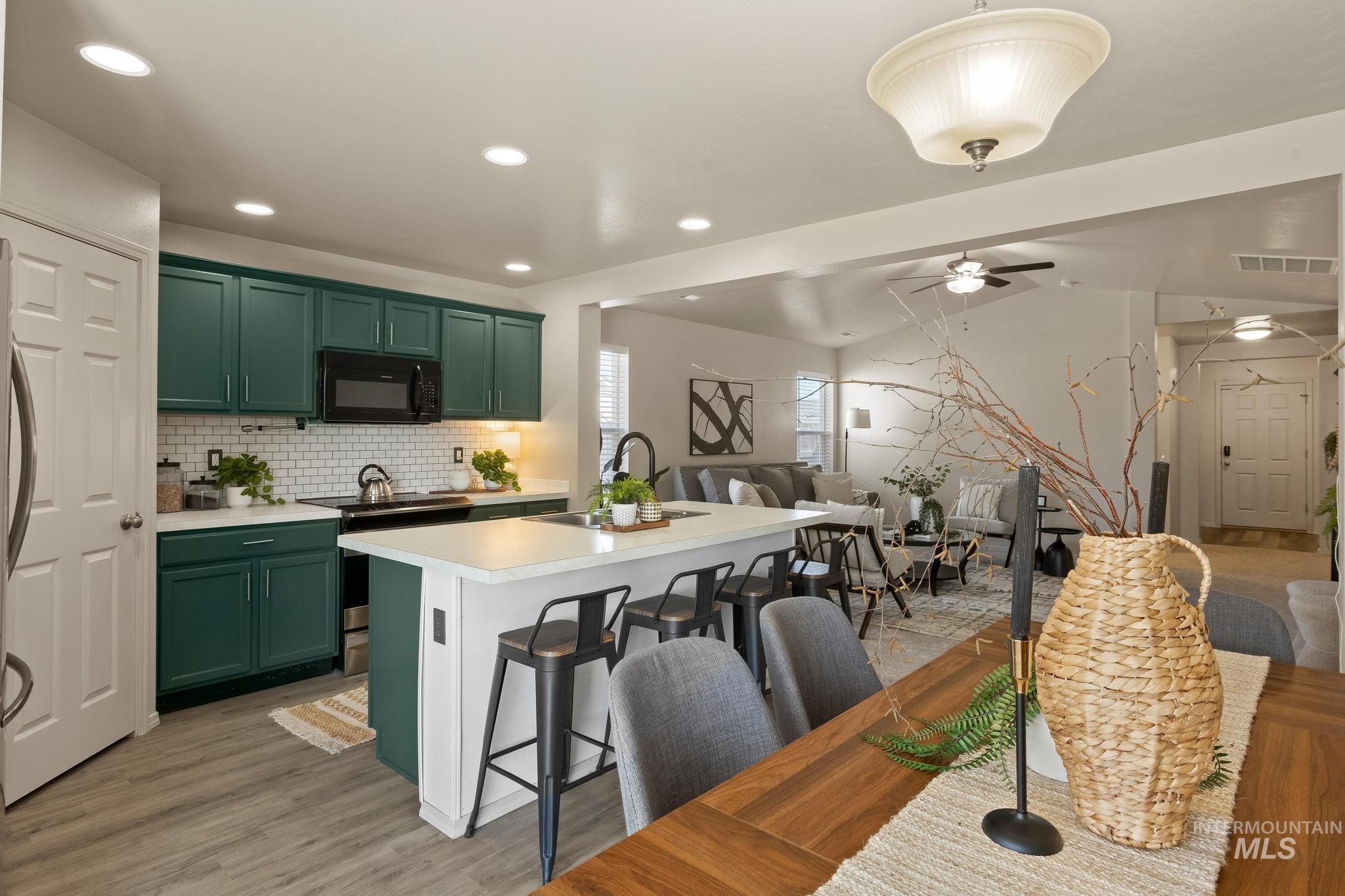 5506 Barkley Way Caldwell, ID 83607 - Photo 17 of 34 Open-concept kitchen featuring dark green cabinetry, white subway tile backsplash, and a central island with bar seating