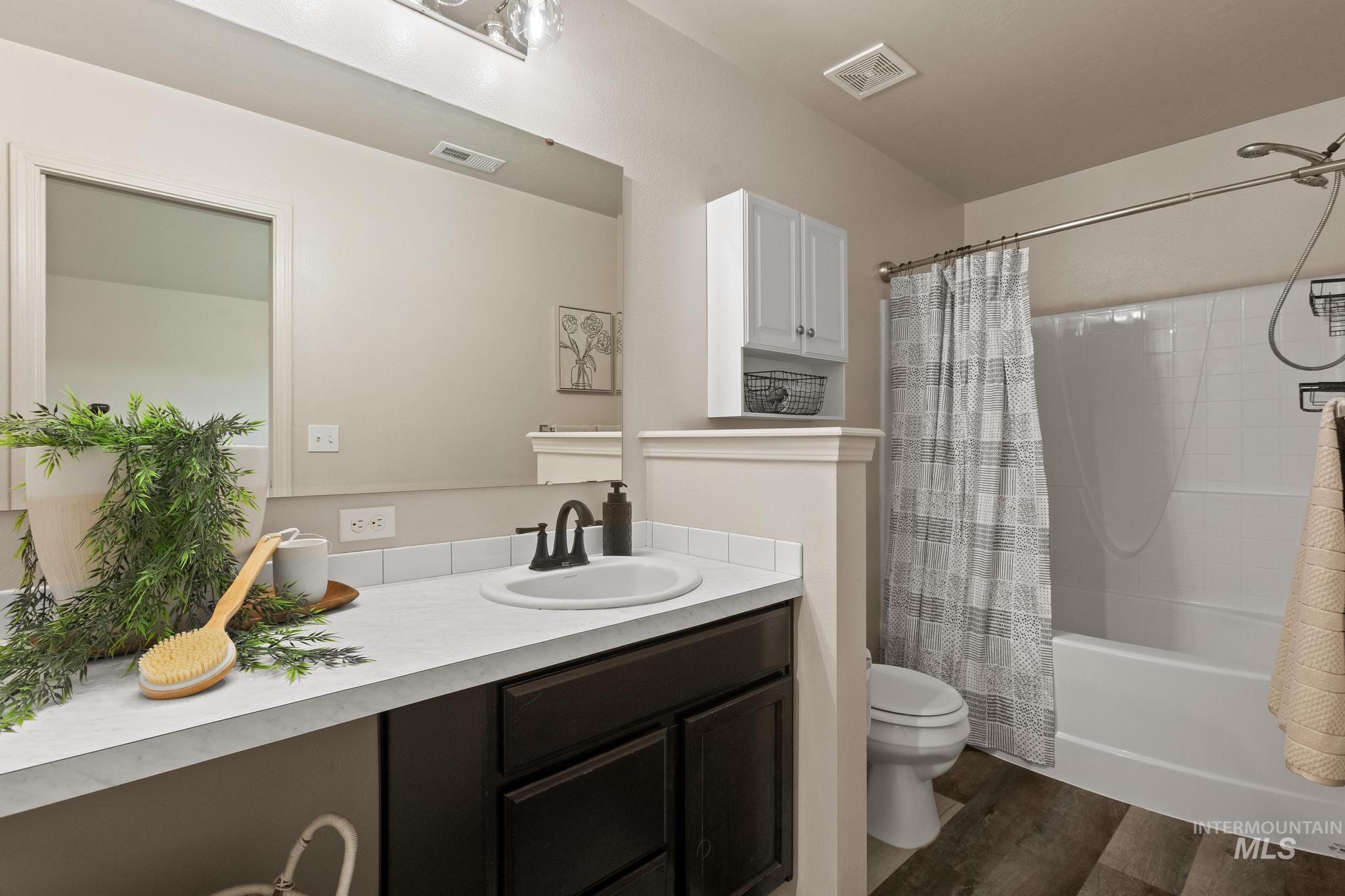 5506 Barkley Way Caldwell, ID 83607 - Photo 23 of 34 Bathroom featuring a dark wood-finish vanity with a single sink and matte black faucet, a large wall-mounted mirror, a built-in bathtub with shower, and wood-finish flooring