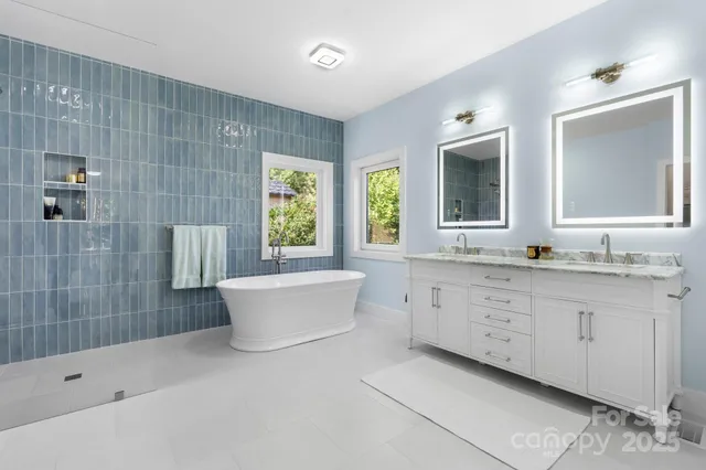 a bathroom with a granite countertop double vanity sink a large mirror a bathtub and next to a window