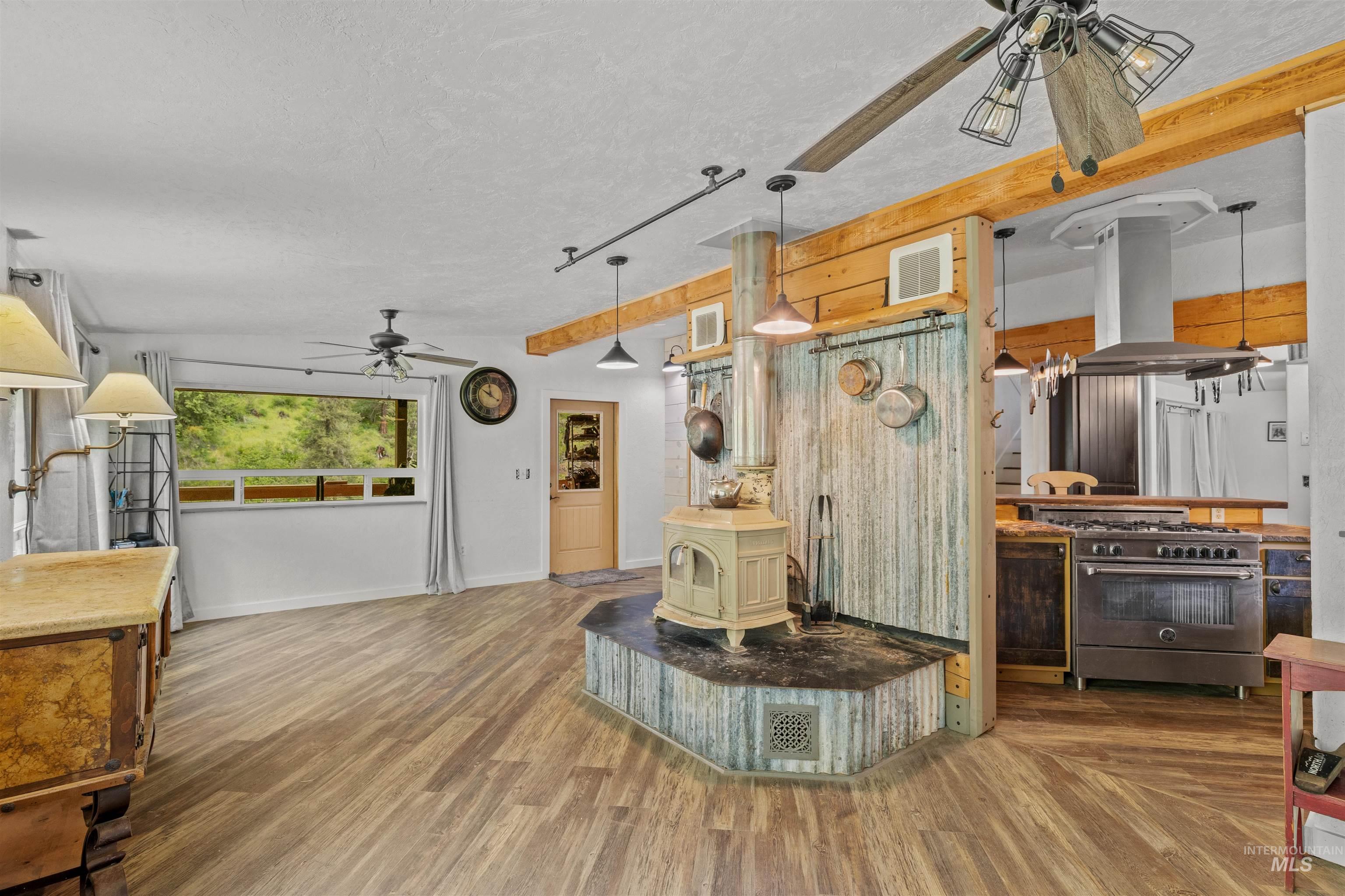 1314 Cedar Ridge Road Kendrick, ID 83537 - Photo 21 of 50 Open-concept living area featuring wood-finish flooring, a central wood-burning stove on a corrugated metal base, and exposed wood beams