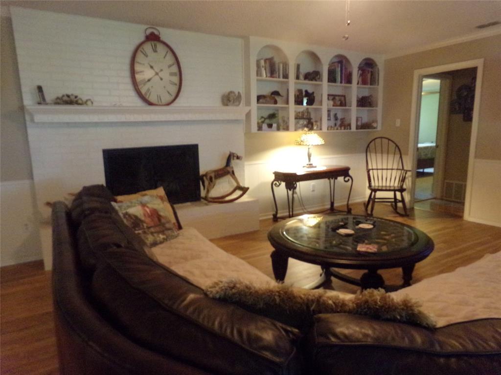 5110 Wedgefield Road Granbury, TX 76049 - Photo 8 of 23 Living area featuring a painted brick fireplace with a mantel, built-in arched shelving, wood-finish flooring, and a doorway leading to another room