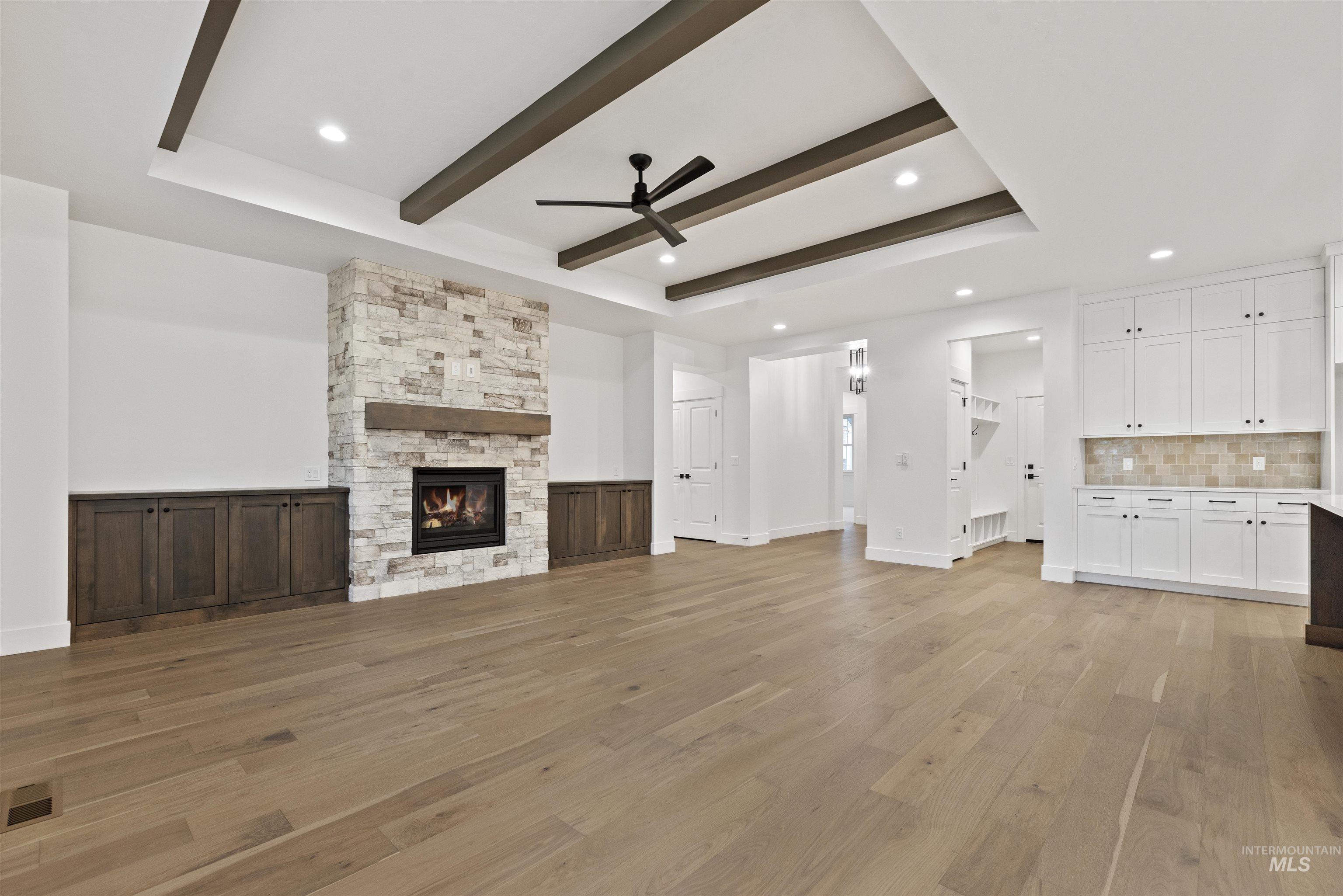 2129 East Blakehurst Street Kuna, ID 83634 - Photo 5 of 34 Unfurnished living room featuring light wood-style flooring, a ceiling fan, a fireplace, a tray ceiling, and recessed lighting