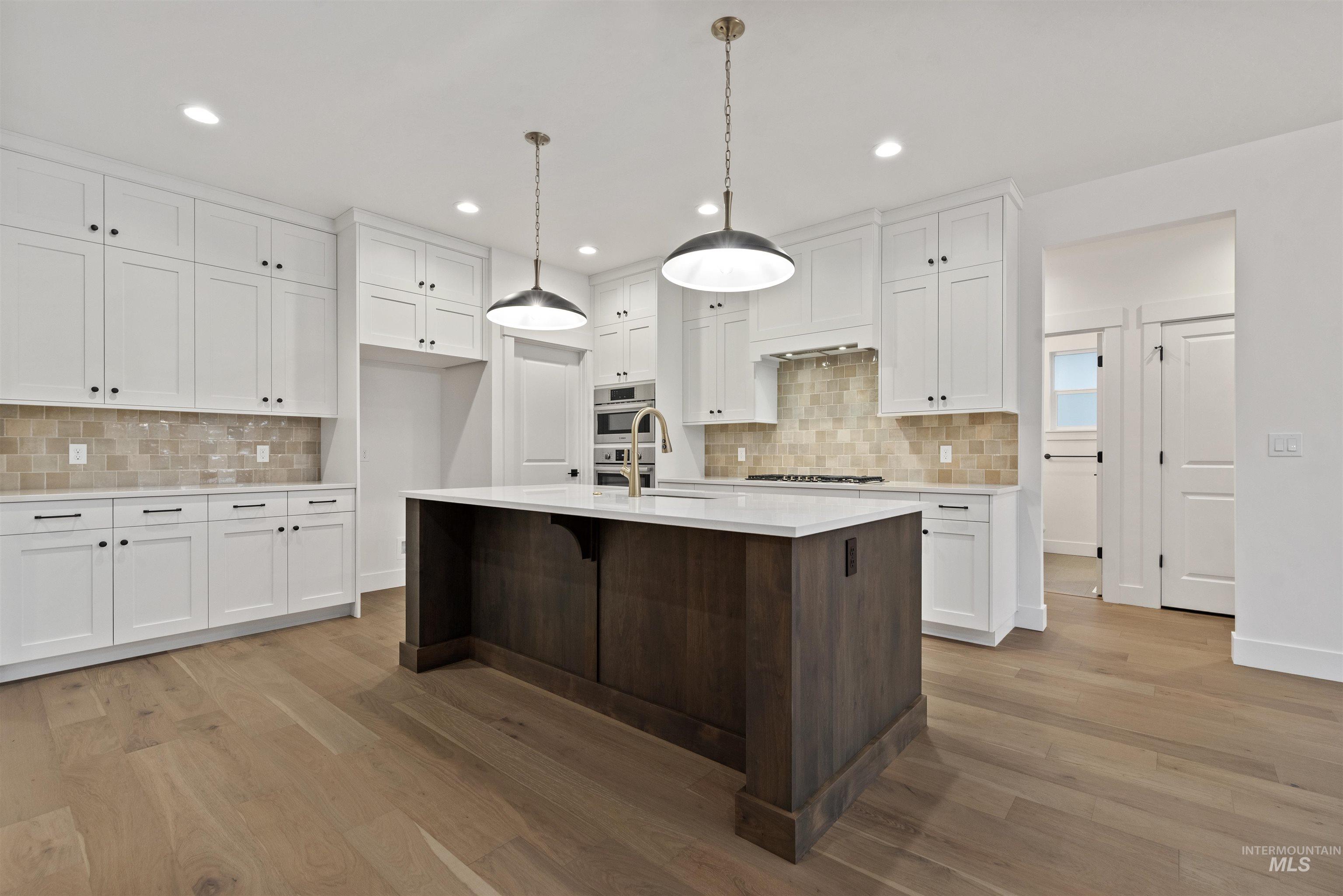 2129 East Blakehurst Street Kuna, ID 83634 - Photo 7 of 34 Kitchen with white cabinetry, dark brown cabinets, a kitchen breakfast bar, a center island with sink, and light wood finished floors