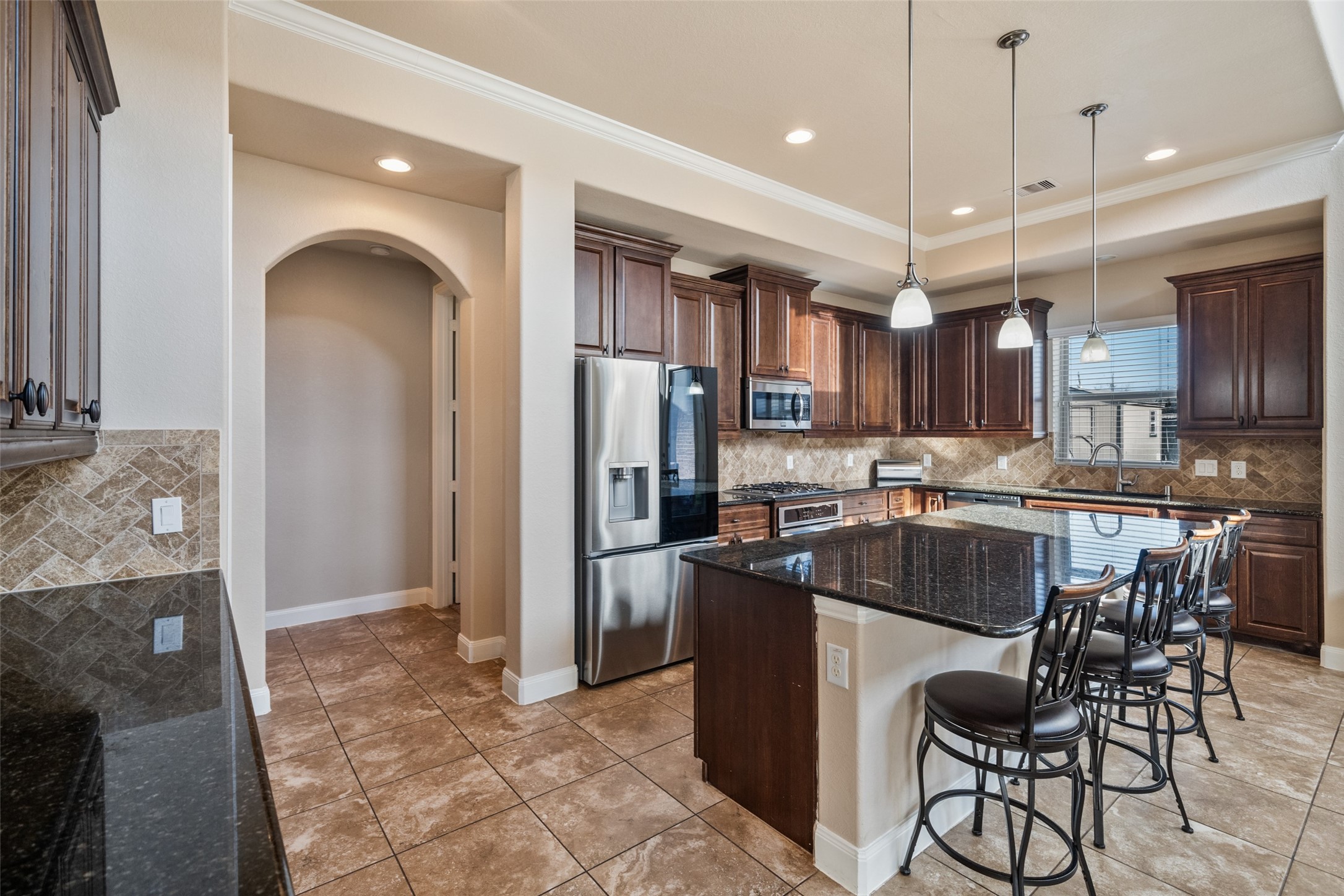 4747 Abercorn Street Rosharon, TX 77583 - Photo 18 of 46 Spacious kitchen with dark wood cabinets, granite countertops, and a central island with bar seating. Features stainless steel appliances, pendant lighting, and a tile floor, creating a modern, elegant atmosphere.