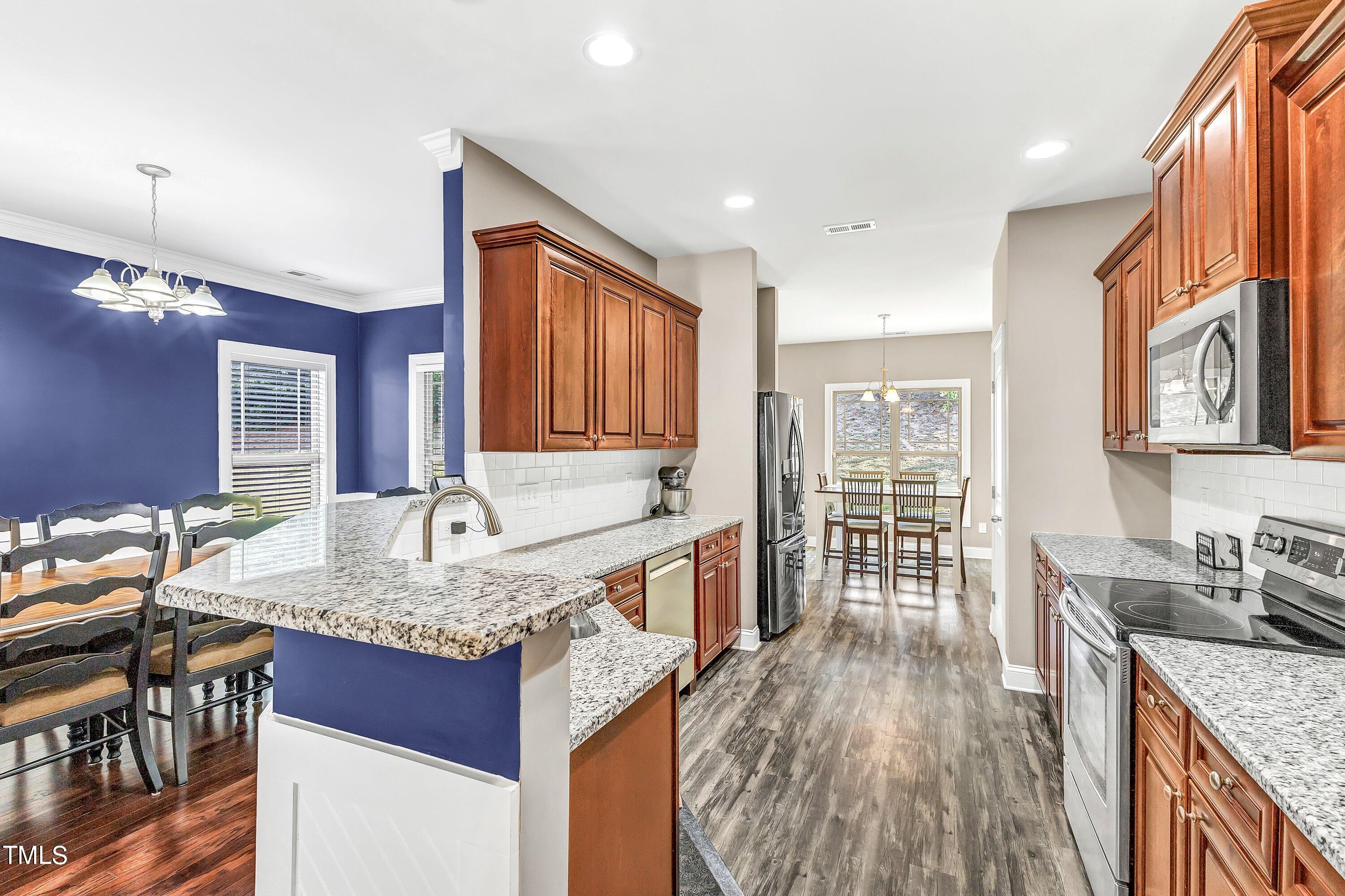 4151 White Kestrel Drive Raleigh, NC 27616 - Photo 12 of 37 a kitchen with granite countertop a stove a sink dishwasher a dining table and chairs with wooden floor