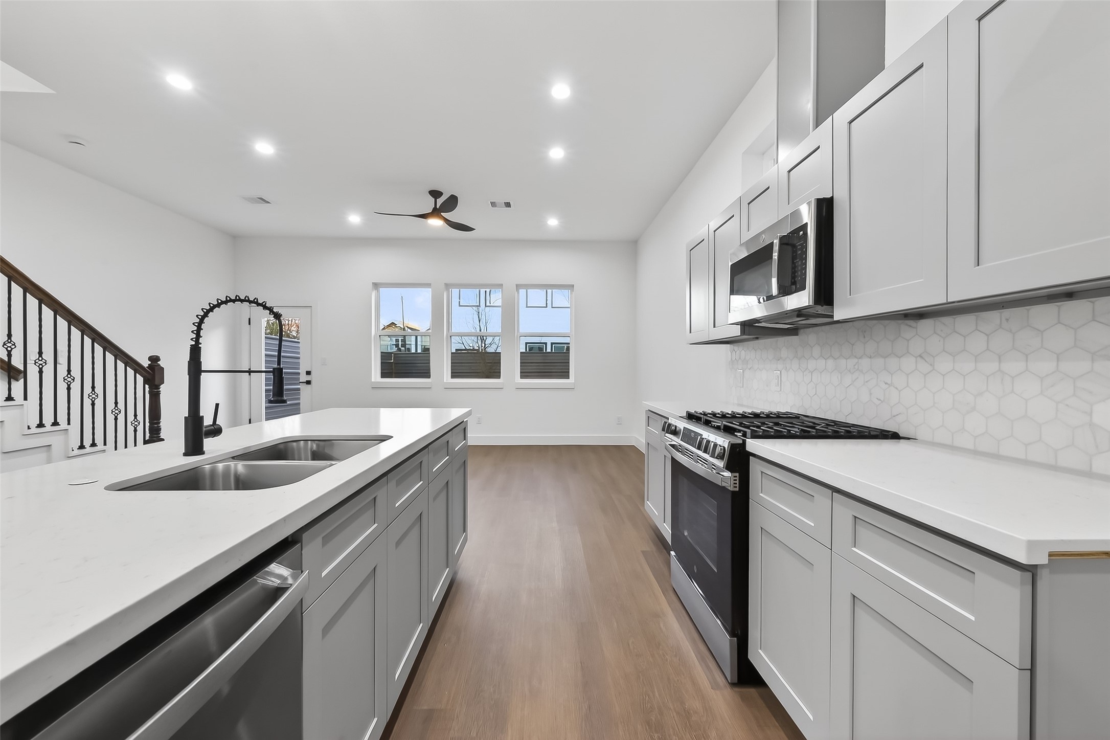 3514 Good Hope Street, Unit B Houston, TX 77021 - Photo 5 of 26 This modern kitchen features sleek gray cabinetry, a spacious island with dual sinks, and stainless steel appliances. The open layout is enhanced by wood flooring, a stylish backsplash, and ample natural light from the large windows.