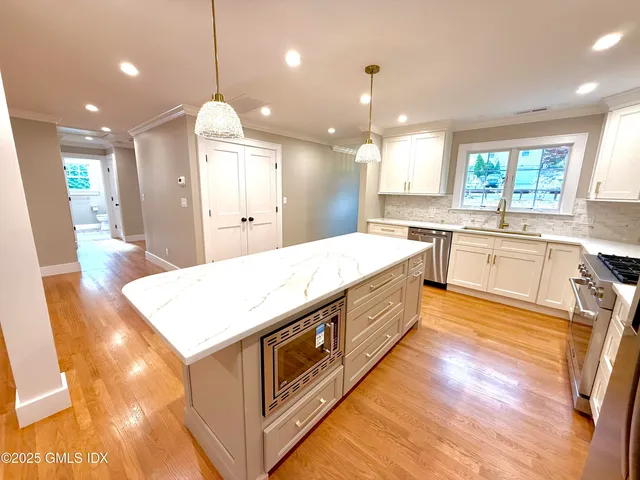 a large white kitchen with a large island oven a sink stainless steel appliances and cabinets