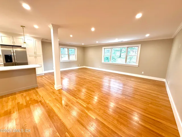a view of an empty room with wooden floor and a kitchen
