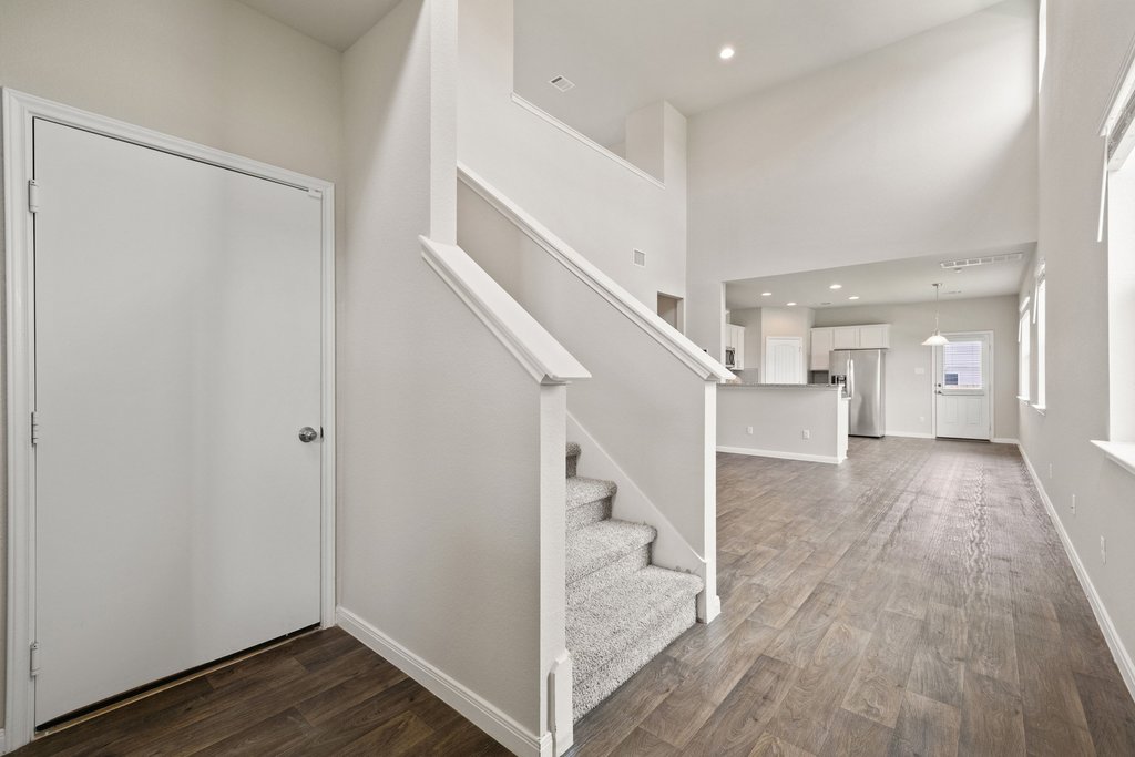102 Ashford Way Georgetown, TX 78626 - Photo 4 of 28 A grand entrance with high ceilings, featuring a carpeted staircase and durable hardwood flooring leading to an open-concept kitchen.