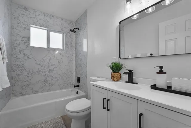 a bathroom with a granite countertop sink a toilet a mirror a bathtub and shower