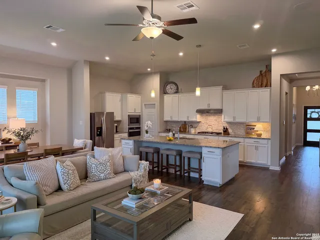 a living room with stainless steel appliances kitchen island granite countertop a couch a dining table and chairs with wooden floor