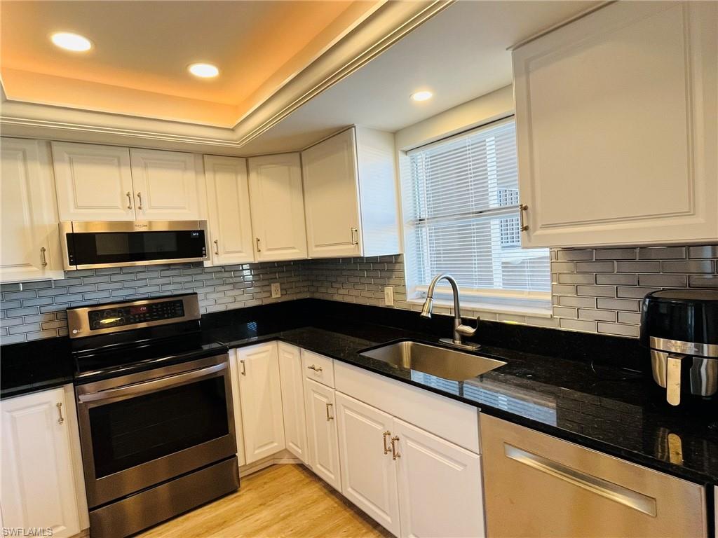 5499 Rattlesnake Hamm Road, Unit 2 Naples, FL 34113 - Photo 5 of 23 Updated Kitchen with stainless steel appliances, white cabinetry, dark stone counters, light wood-style flooring, and recessed lighting