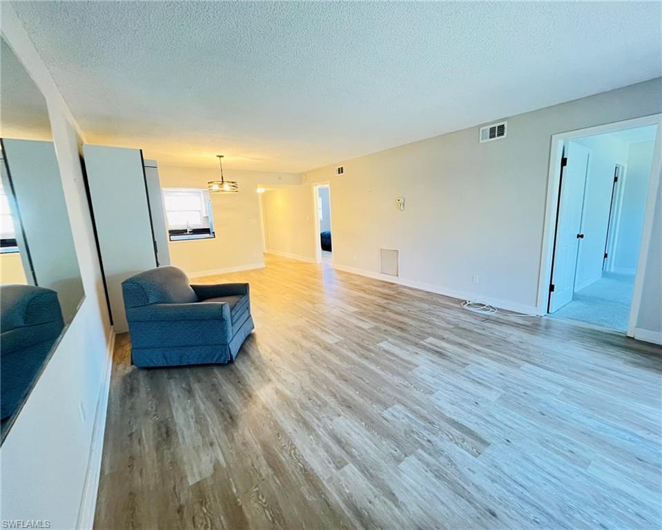 5499 Rattlesnake Hamm Road, Unit 2 Naples, FL 34113 - Photo 9 of 23 Unfurnished living room with light wood-type flooring, a textured ceiling, and a chandelier