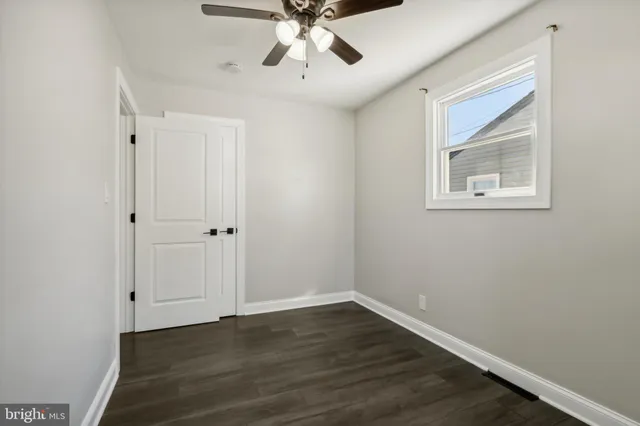 a view of an empty room with wooden floor and a ceiling fan