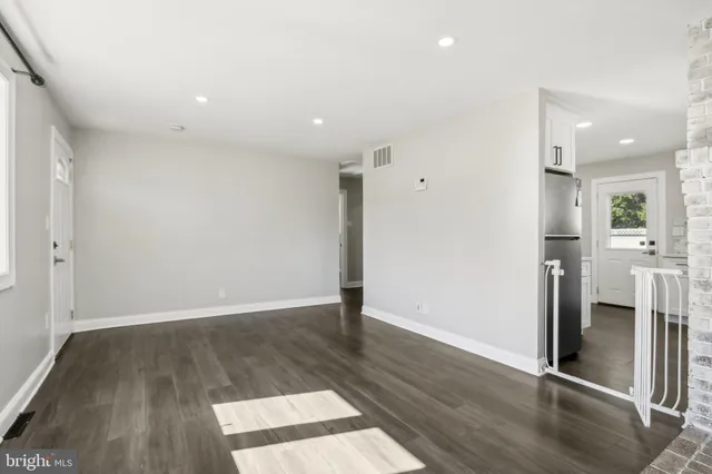 an empty room with wooden floor and a kitchen