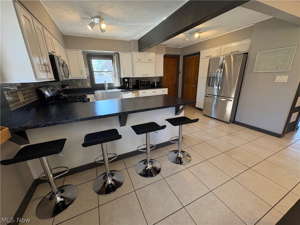 17583 Shurmer Road Strongsville, OH 44136 - Photo 17 of 50 Kitchen featuring a spacious peninsula with seating, light cabinetry, dark stone-look countertops, subway tile backsplash, and stainless steel appliances