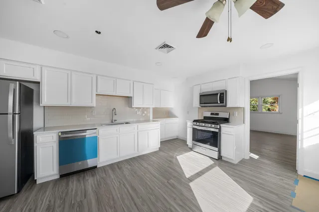 a kitchen with stainless steel appliances a stove a sink dishwasher a refrigerator and white cabinets with wooden floor