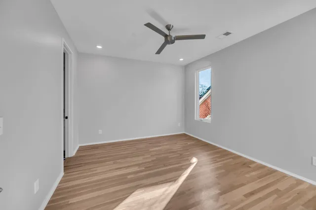 an empty room with wooden floor ceiling fan and windows