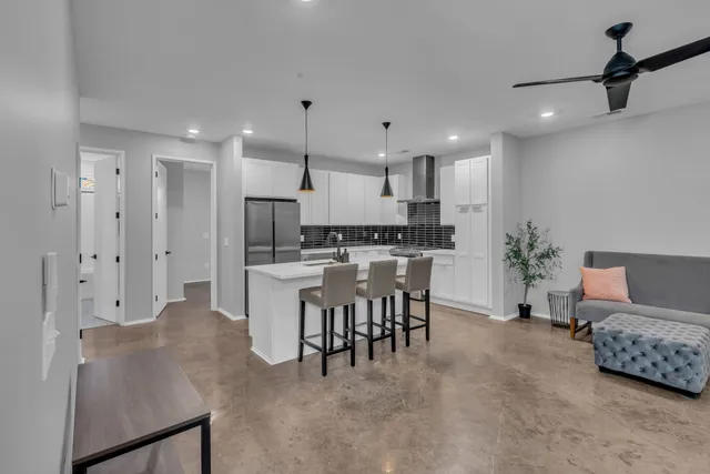 a large white kitchen with stainless steel appliances kitchen island granite countertop a refrigerator a stove a sink a dining table and chairs