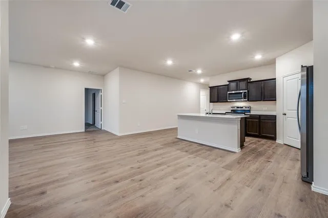 a large kitchen with kitchen island a stove a sink dishwasher a refrigerator and white cabinets with wooden floor