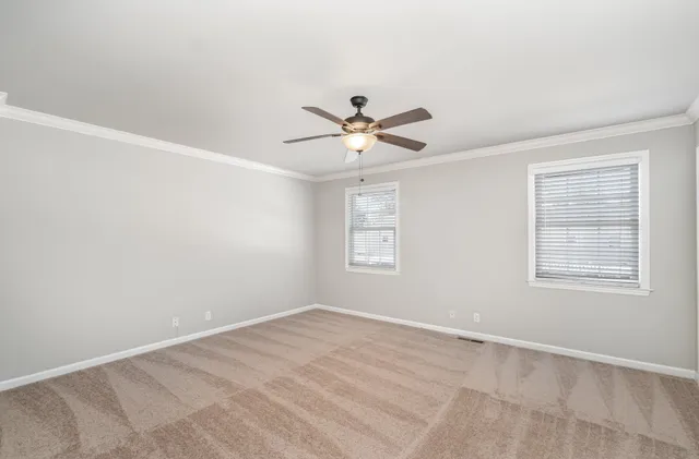 an empty room with chandelier fan and windows