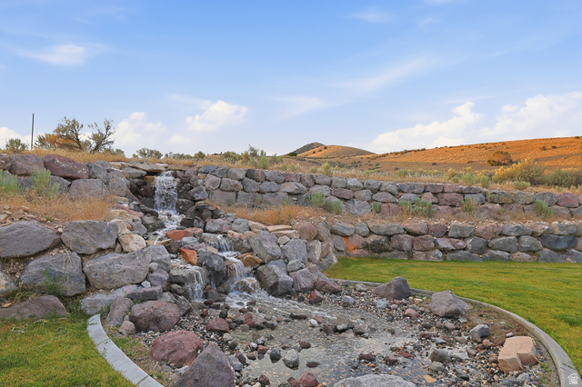2056 West Ridgeline Road Stockton, UT 84071 - Photo 7 of 50 Tiered rock wall landscaping featuring a multi-level water feature, natural stone boulders, and a curved concrete border