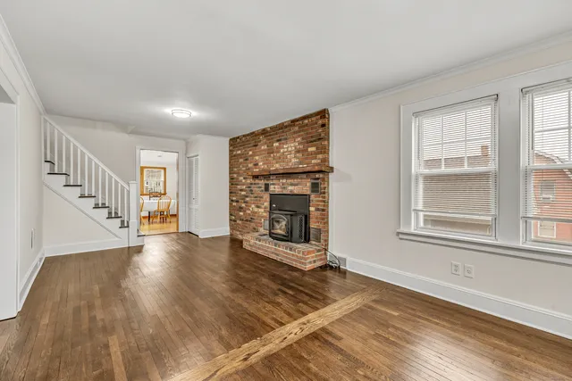 a view of an empty room with wooden floor fireplace and a window