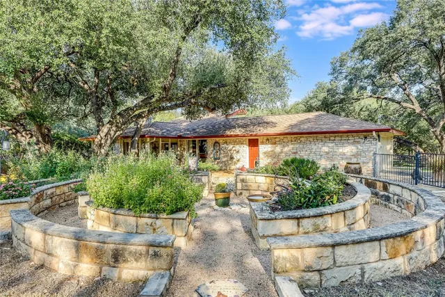 a view of a house with a yard plants and large tree