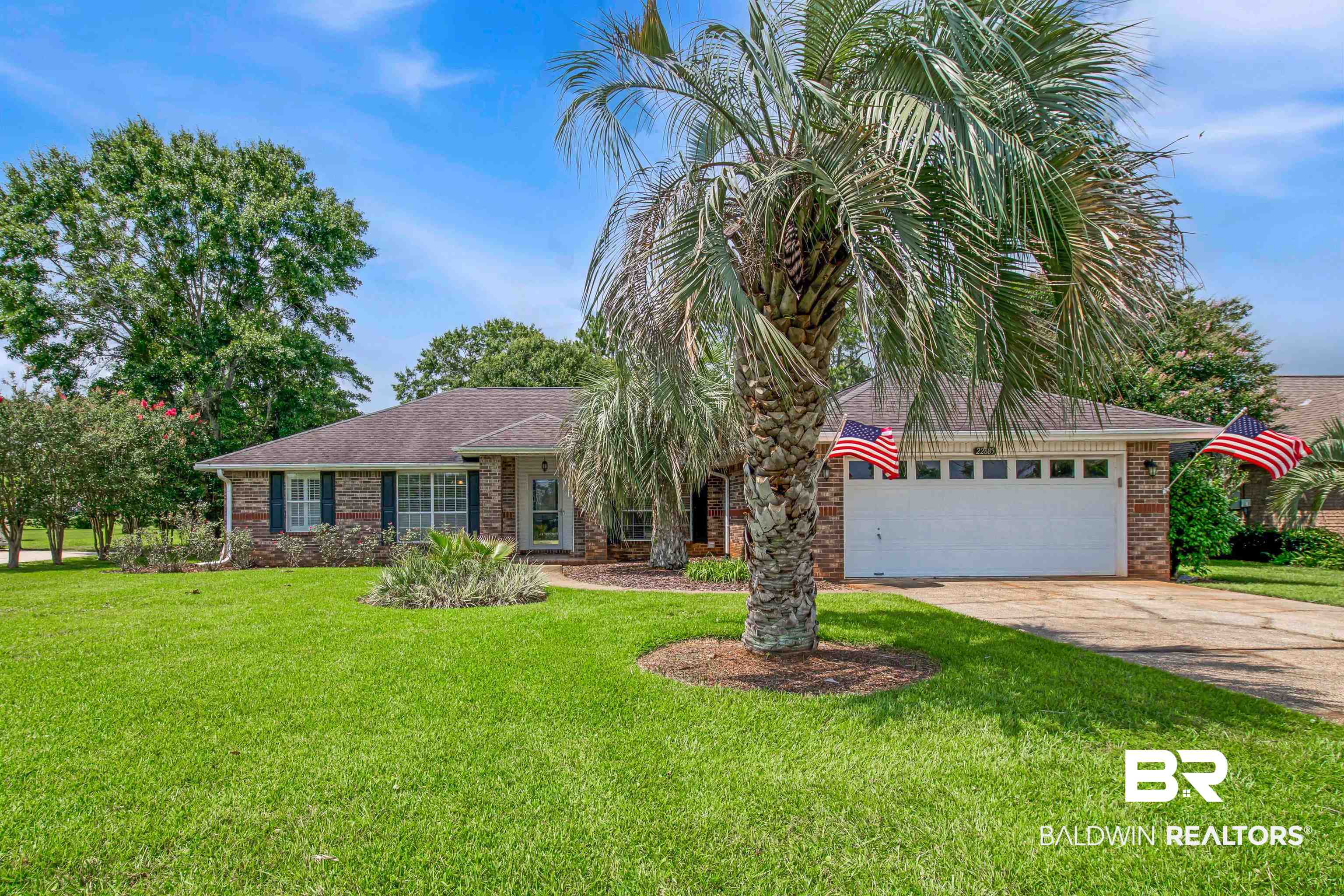 22685 County Road 12 Foley, AL 36535 - Photo 6 of 89 Brick exterior with a white garage door, featuring mature palm trees and a manicured lawn