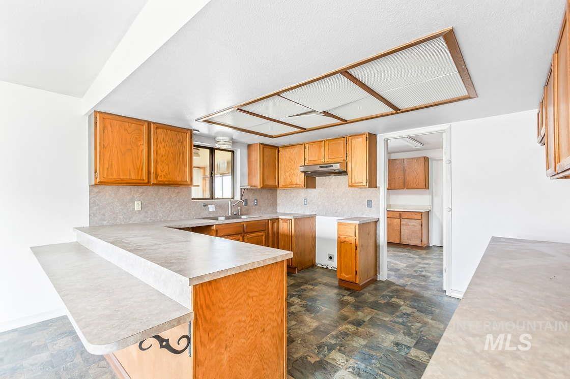 255 3 Bear Creek Road Kendrick, ID 83537 - Photo 16 of 44 Kitchen with a peninsula, tasteful backsplash, light countertops, brown cabinets, and stone finish floors