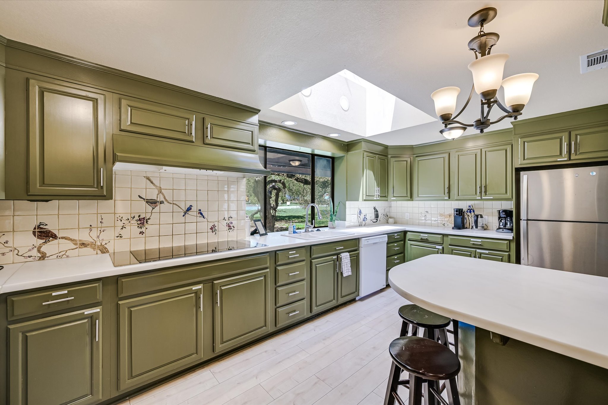 411 Whitetail Ridge Austin, TX 78737 - Photo 9 of 38 Kitchen with a skylight, green cabinetry, freestanding refrigerator, dishwasher, and a kitchen bar