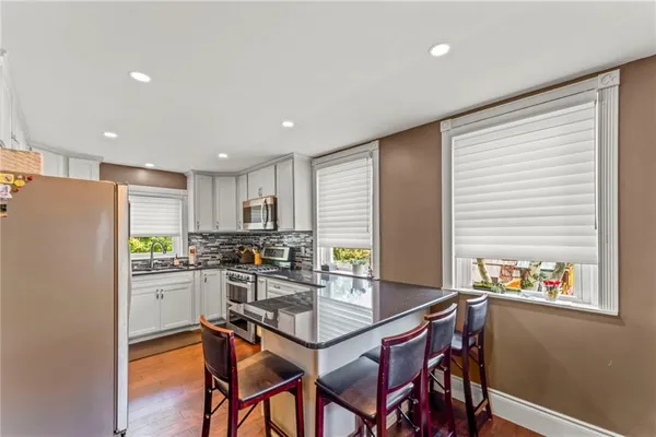 a kitchen with stainless steel appliances granite countertop a stove a refrigerator a microwave a sink and white cabinets with wooden floor