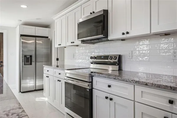 a kitchen with stainless steel appliances granite countertop a refrigerator a stove a sink and white cabinets