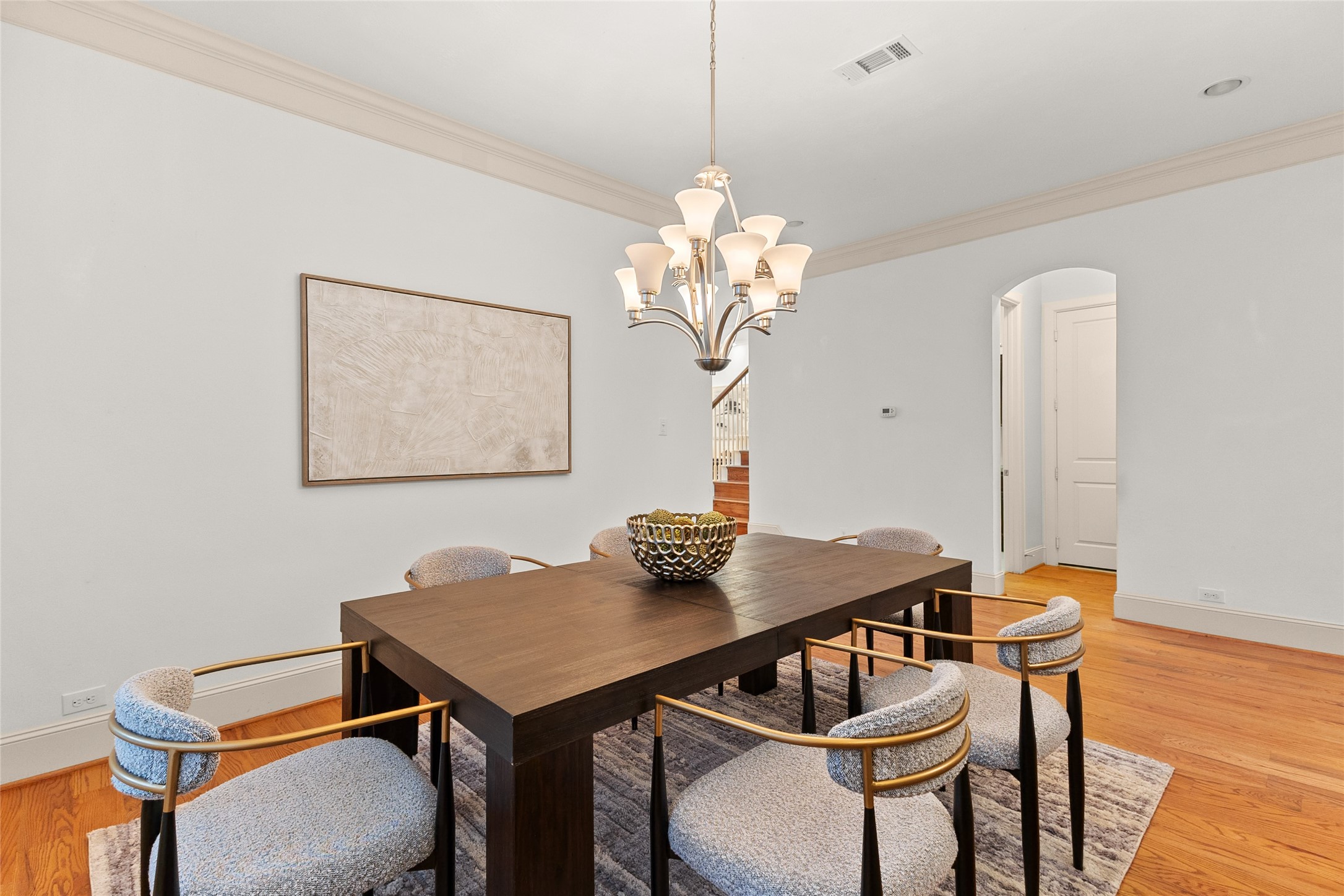 3302 Rochdale Street Houston, TX 77025 - Photo 15 of 50 This second view of the dining room highlights its open flow into the entryway, with a glimpse of the staircase adding to the home's sense of connectivity. A statement chandelier, rich hardwood floors, and crown molding carry the same elegant details seen throughout the space. It's a versatile room that works just as well for everyday meals as it does for entertaining.