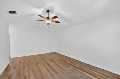 an empty room with wooden floor fan and windows