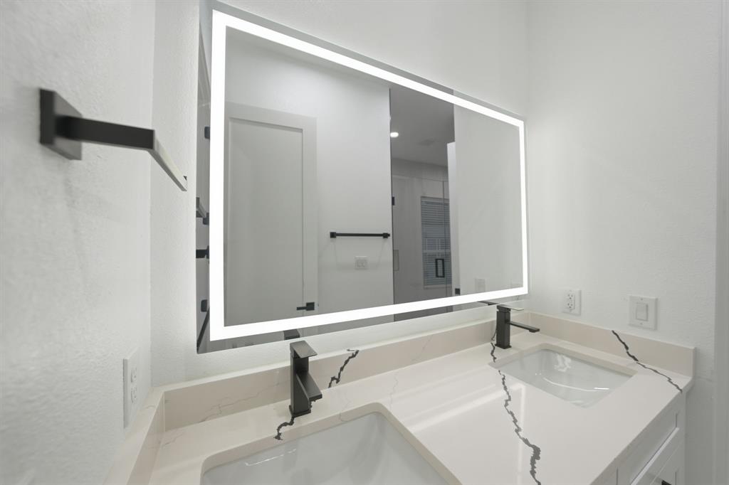 306 East 7th Street Dallas, TX 75203 - Photo 17 of 22 Dual vanity with integrated sinks, light-toned countertop featuring distinctive veining, matte black fixtures, and an illuminated mirror