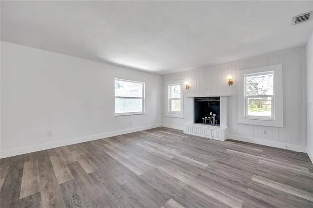an empty room with windows a fireplace and wooden floor