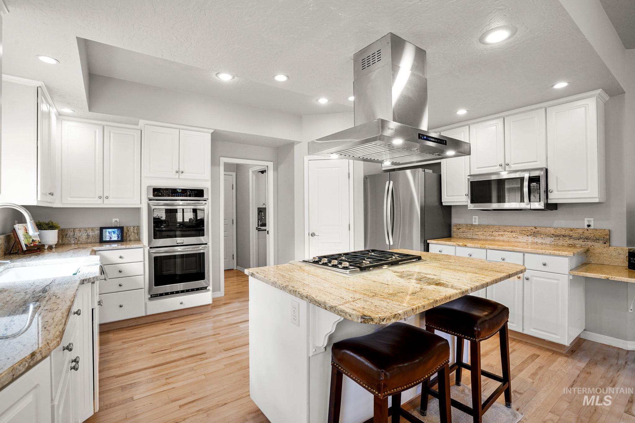 5790 North Wellspring Way Boise, ID 83713 - Photo 12 of 41 Kitchen with white cabinetry, a kitchen island, light wood finished floors, stainless steel appliances, and light stone countertops