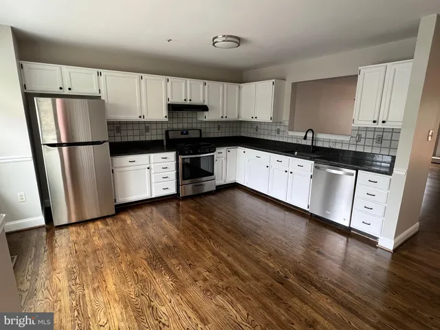 a kitchen with granite countertop a refrigerator a sink and white cabinets