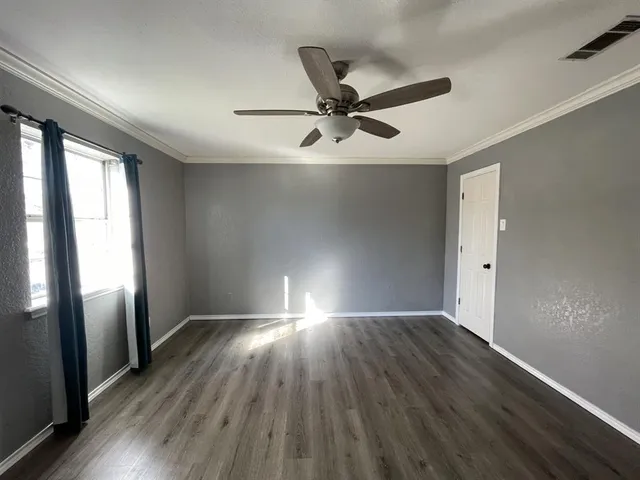 an empty room with wooden floor fan and windows